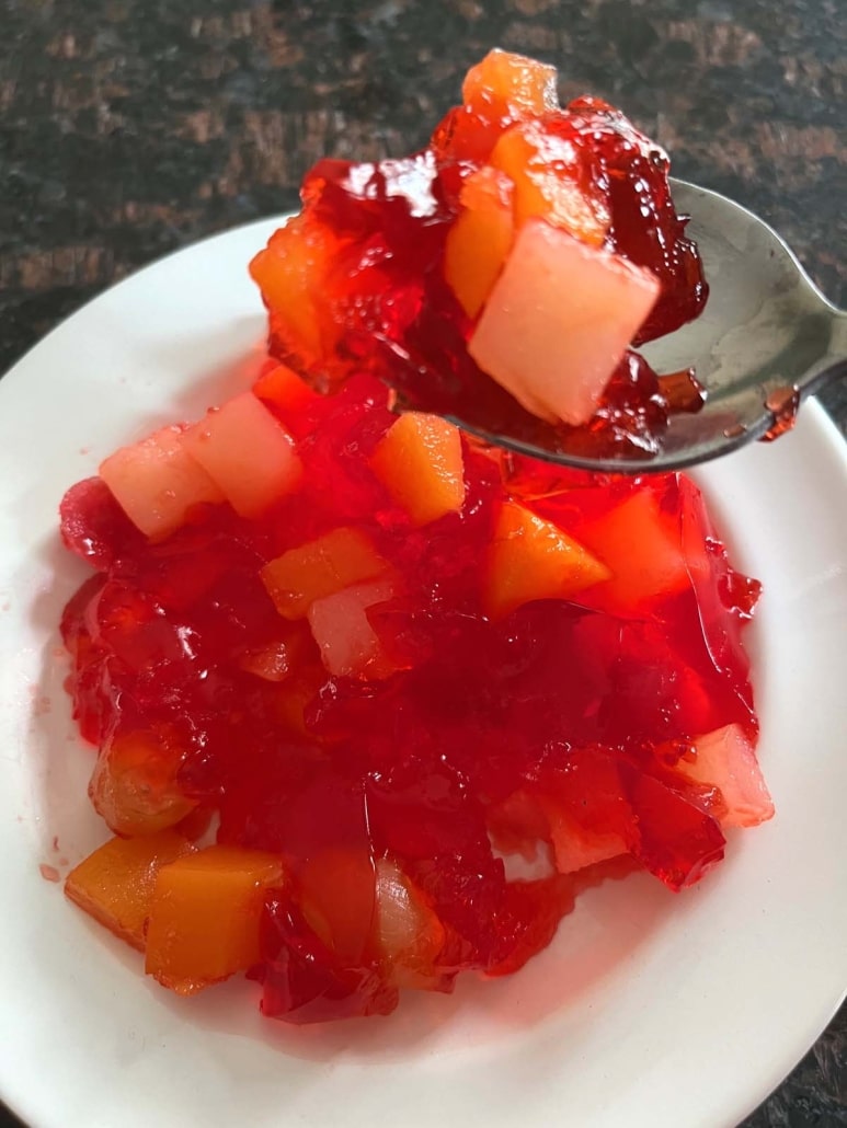 spoonful of yummy Jello With Fruit Cocktail above a plate of Jello