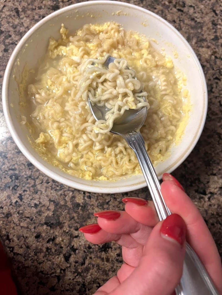 hand holding spoonful of egg and ramen soup