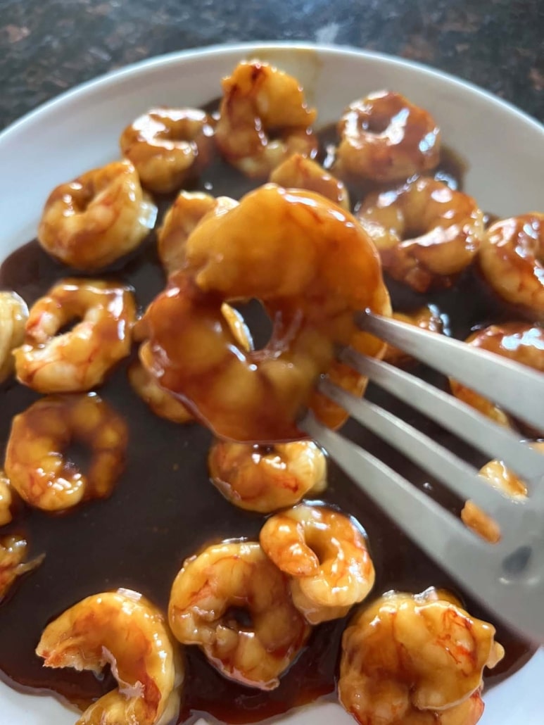 fork with teriyaki shrimp, in front of a plate of shrimp