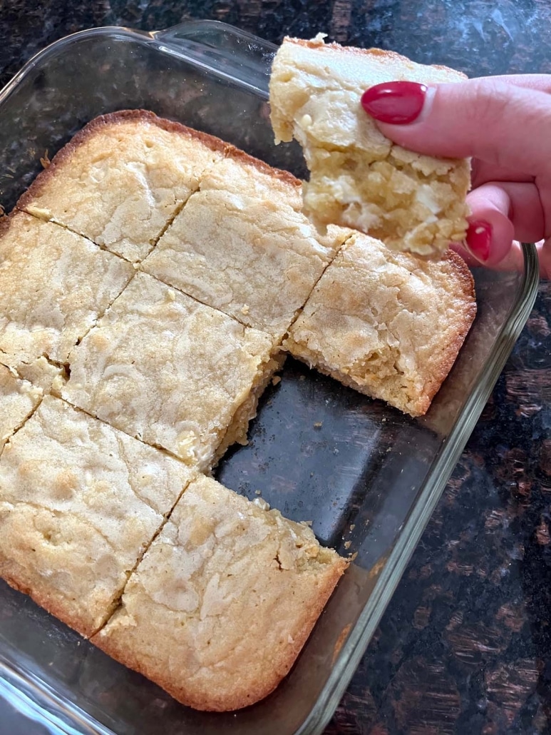 hand holding a moist and chewy vanilla brownie next to a pan of vanilla brownies