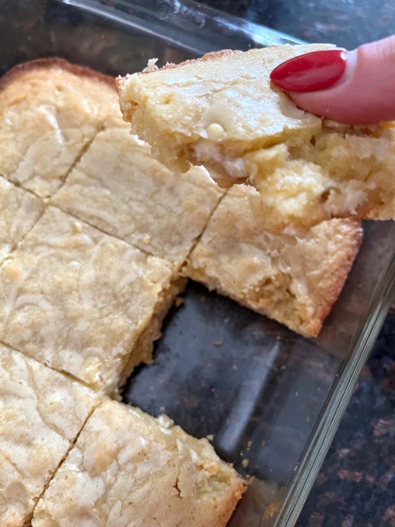 hand holding a homemade vanilla brownie next to a pan of vanilla brownies