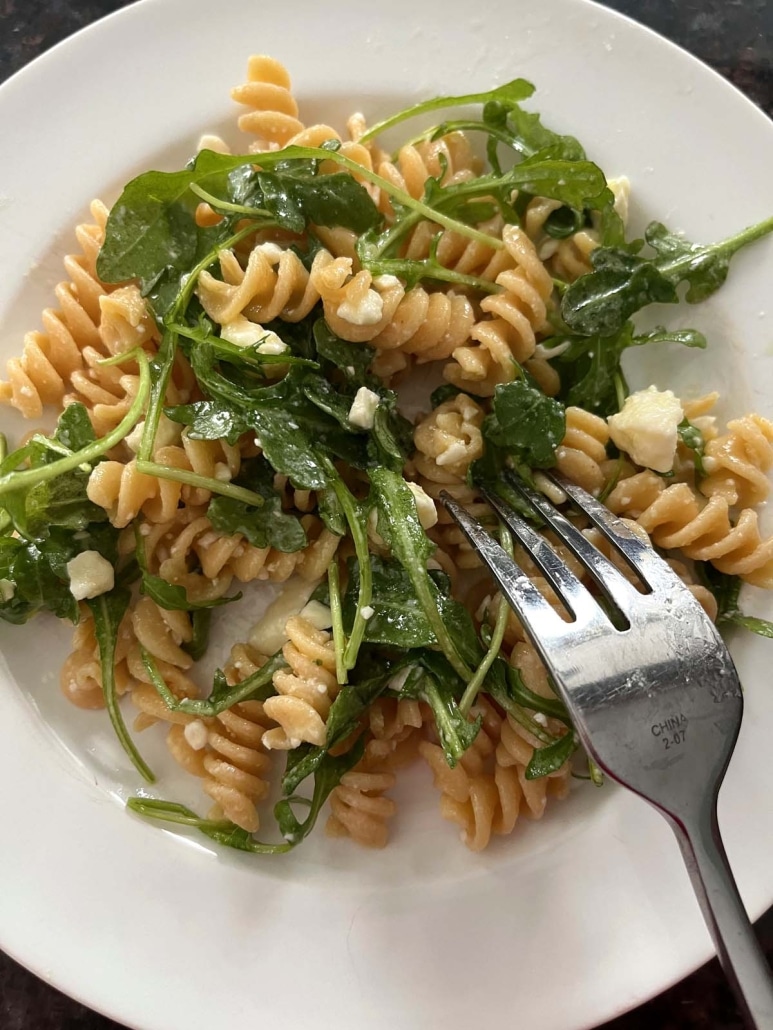 fork in freshly prepared Arugula Pasta Salad with olive oil and lemon dressing