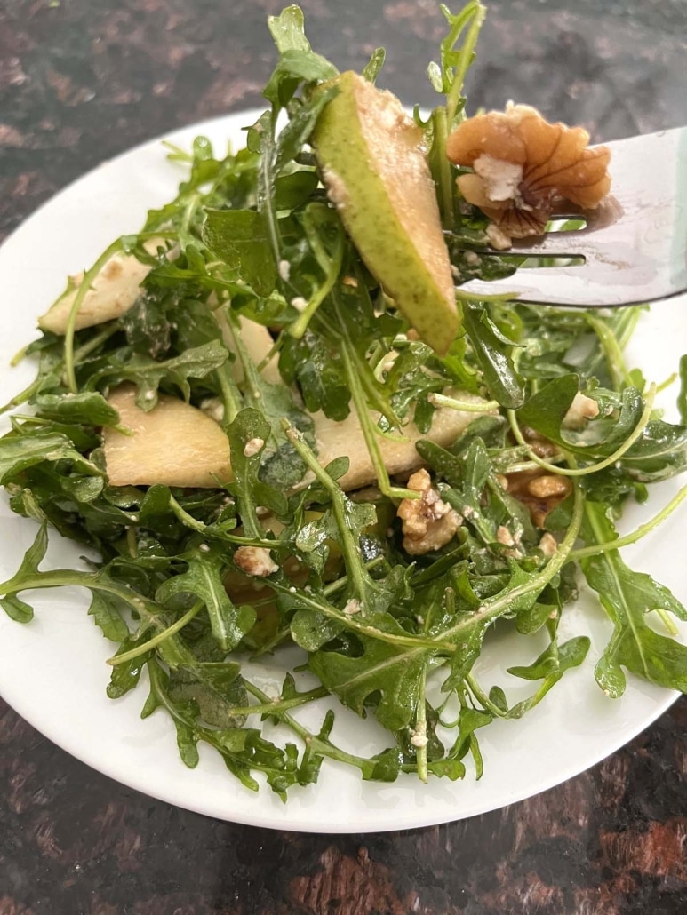 fork grabbing bit of side salad Arugula Pear And Goat Cheese Salad