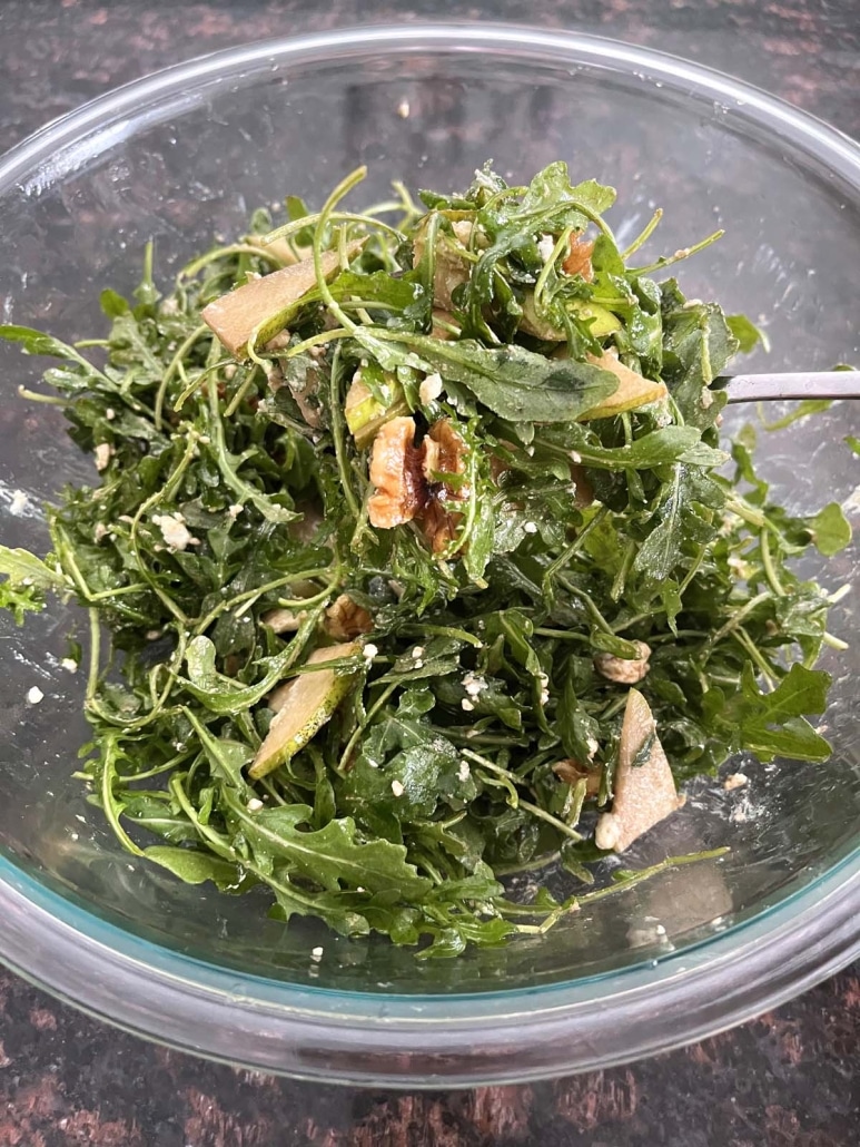 tossing Arugula Pear And Goat Cheese Salad in a big salad bowl