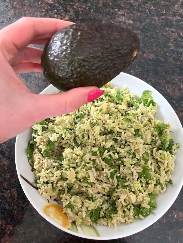 hand holding an avocado above a bowl of Avocado Rice