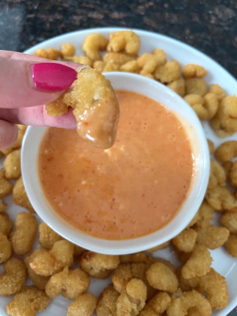 hand dipping a popcorn shrimp into bang bang sauce