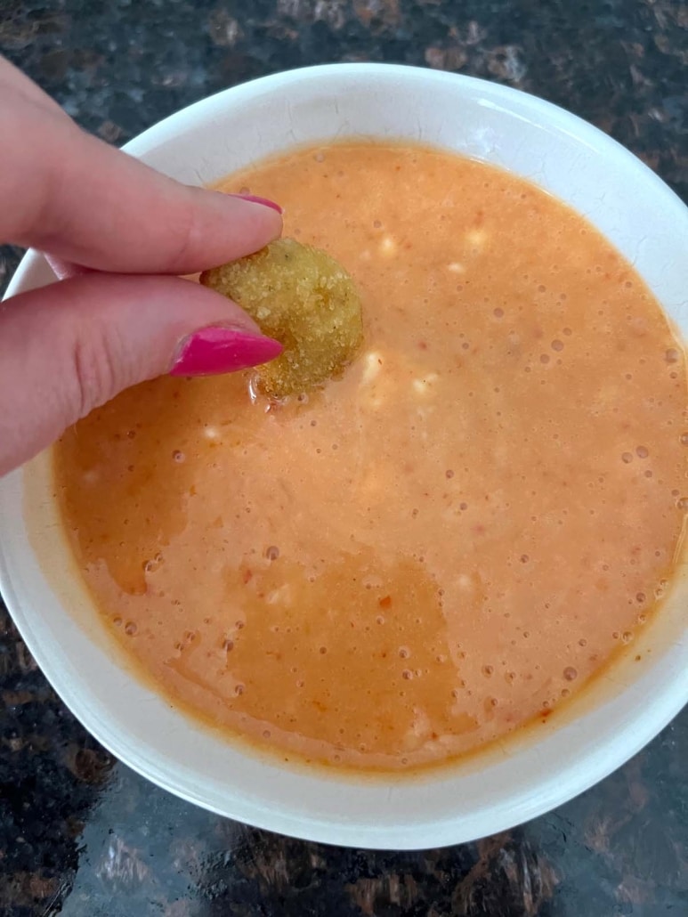 hand dipping a tasty popcorn shrimp into appetizer bang bang sauce