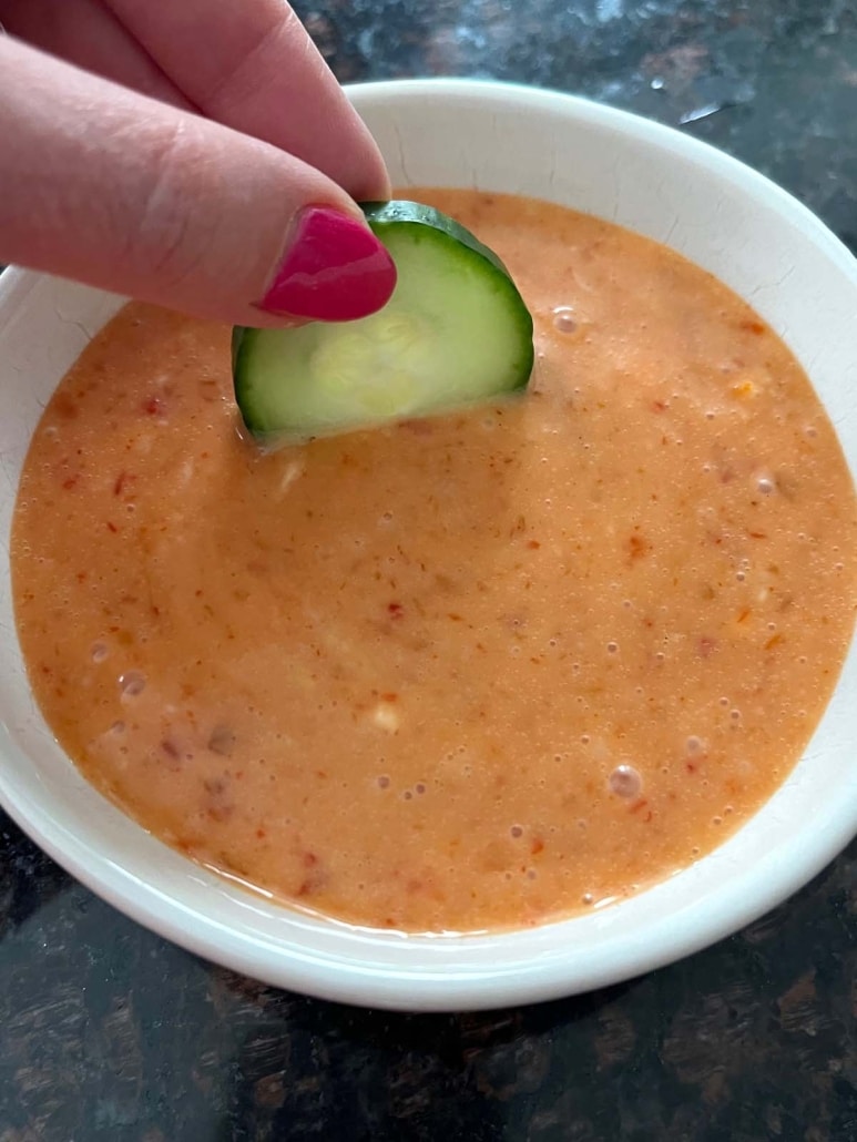 hand dipping a sliced cucumber into creamy bang bang sauce