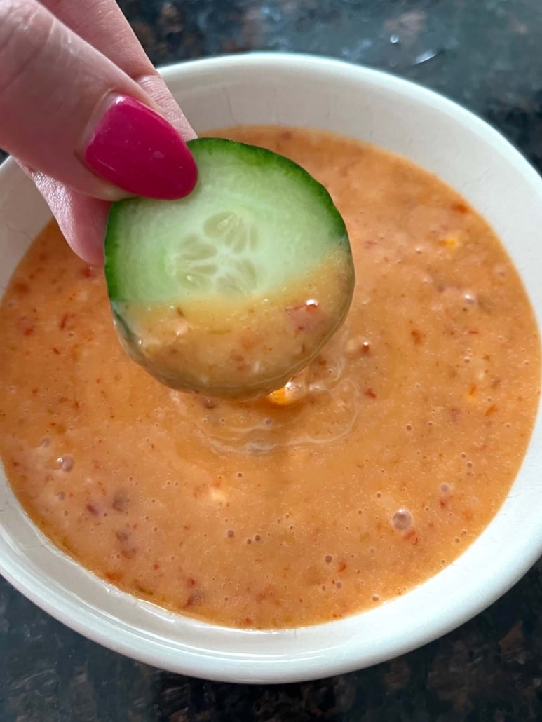 hand dipping slice of cucumber into bang bang sauce