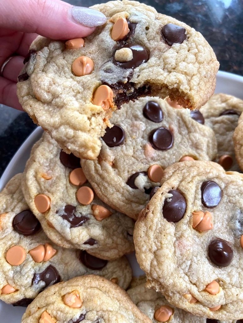 hand holding Caramel Chocolate Chip Cookie in front of plate of Caramel Chocolate Chip Cookies