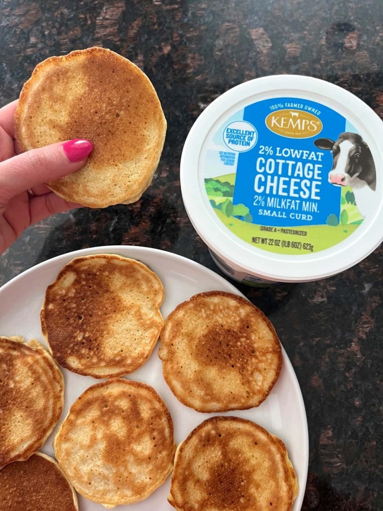 hand holding a Cottage Cheese Pancake next to a container of cottage cheese