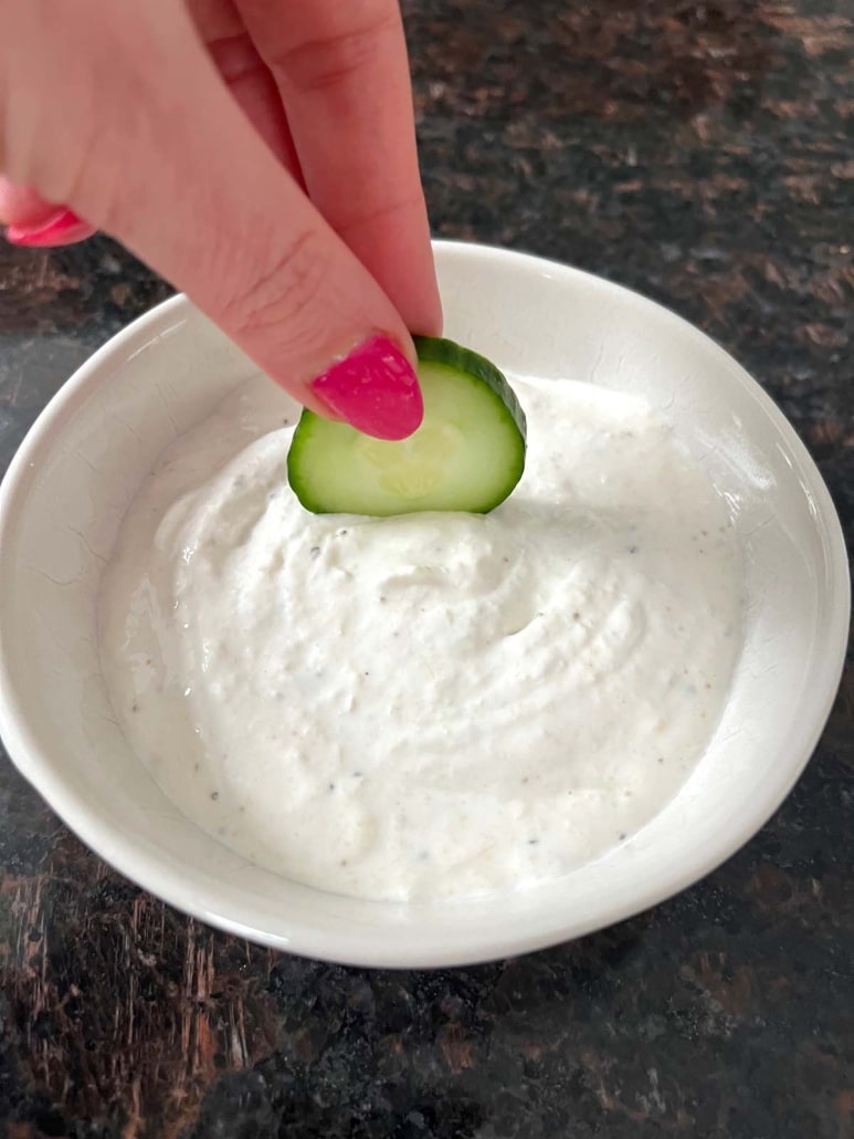 hand dipping cucumber slice into easy appetizer dip Creamy Horseradish Sauce