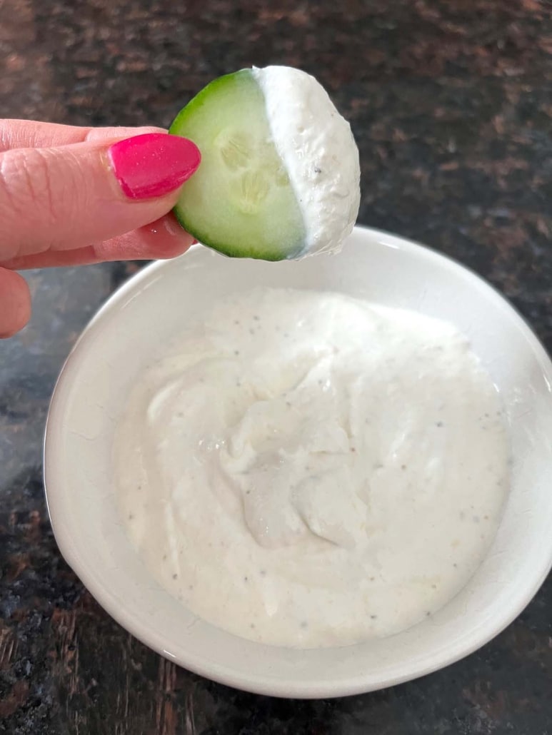 hand holding cucumber slice dipped in Creamy Horseradish Sauce