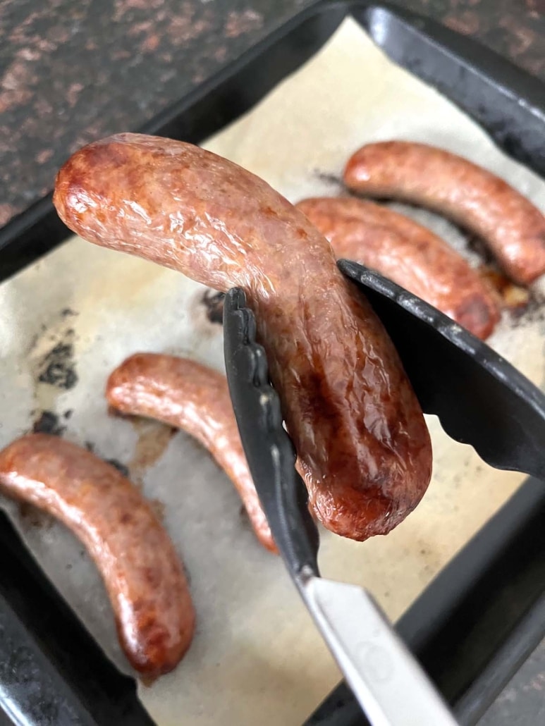 tongs holding a brat baked in the oven