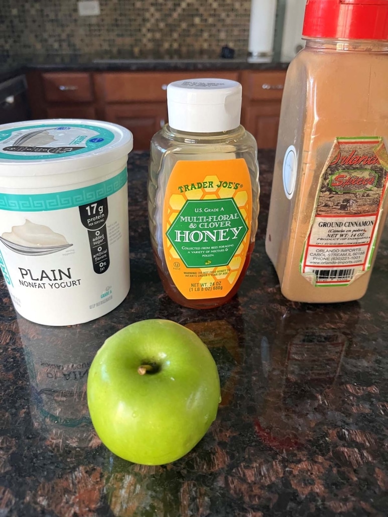 an apple, container of Greek yogurt, honey, and cinnamon on a countertop