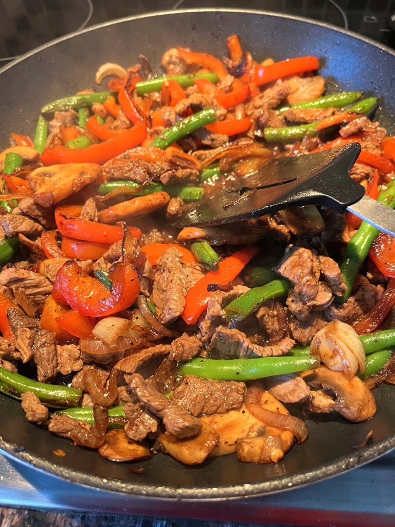 spatula mixing up tender sirloin steak strips and chopped veggies