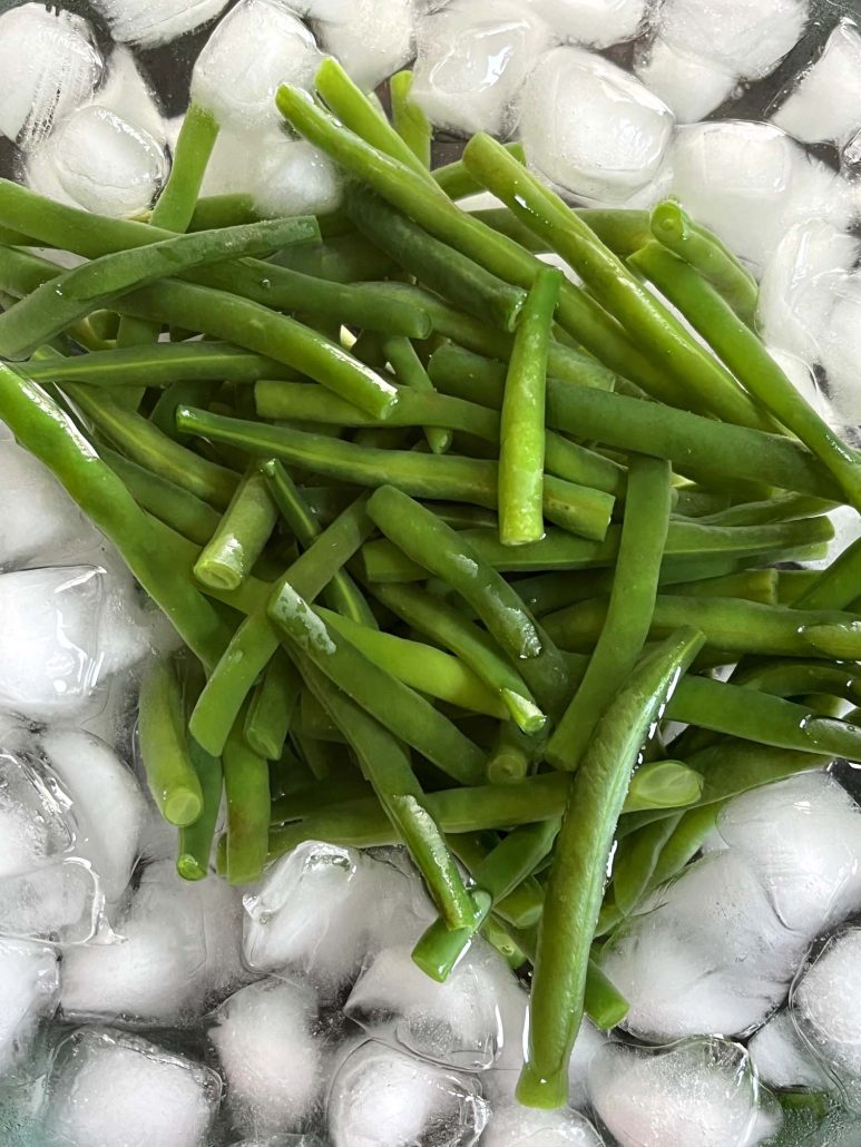 freshly boiled green beans cooling off in a bowl of ice water