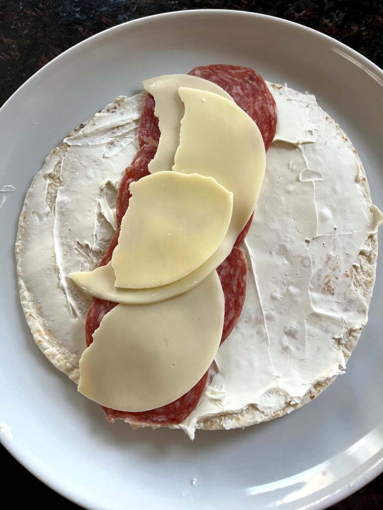 tortilla topped with cream cheese, salami, and provolone cheese