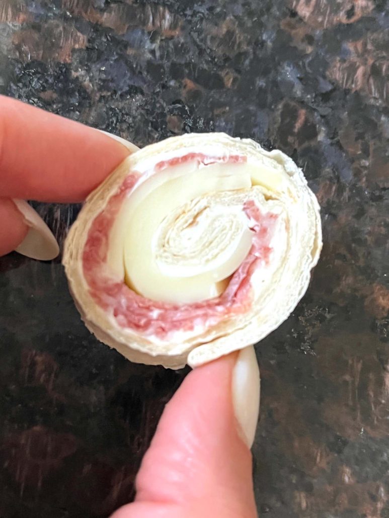 hand holding a salami and cheese roll-up