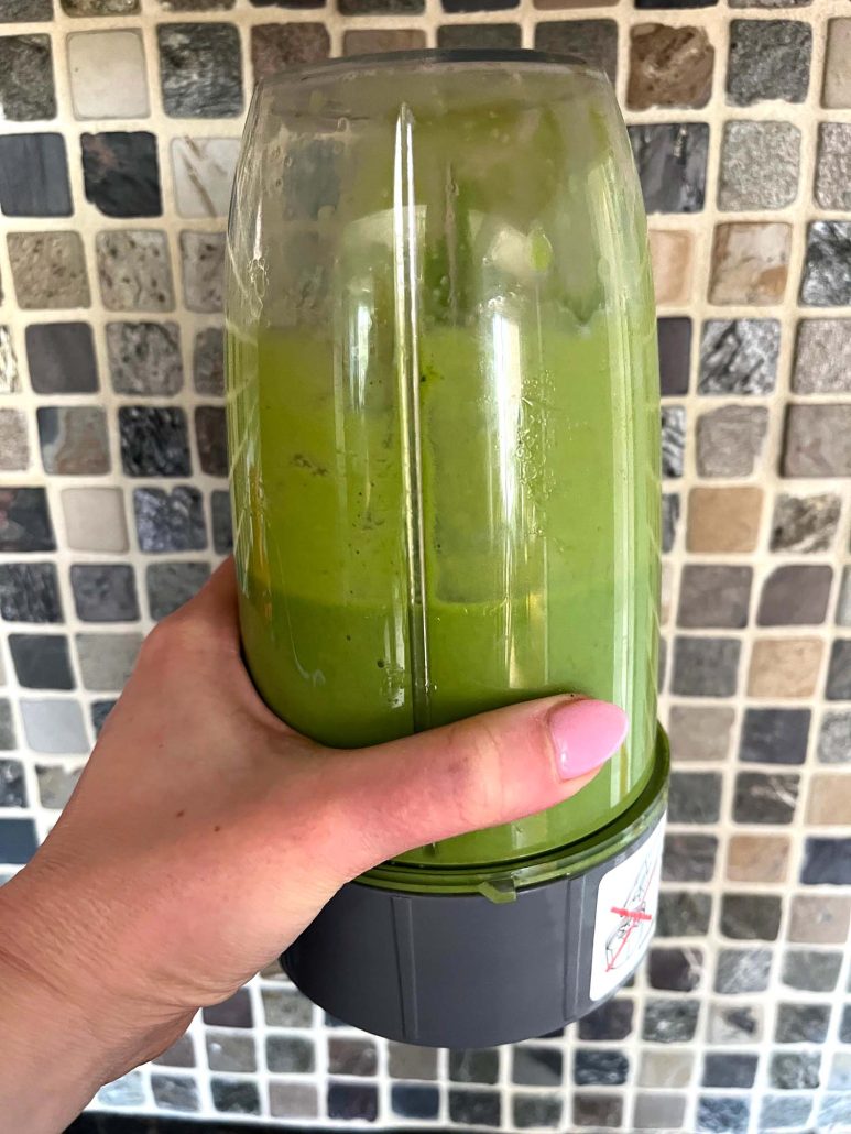 hand holding a blender cup with Mango Spinach Smoothie inside