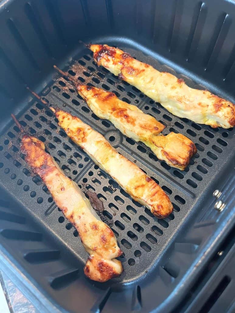 A close-up of four golden brown chicken skewers inside an air fryer basket. 