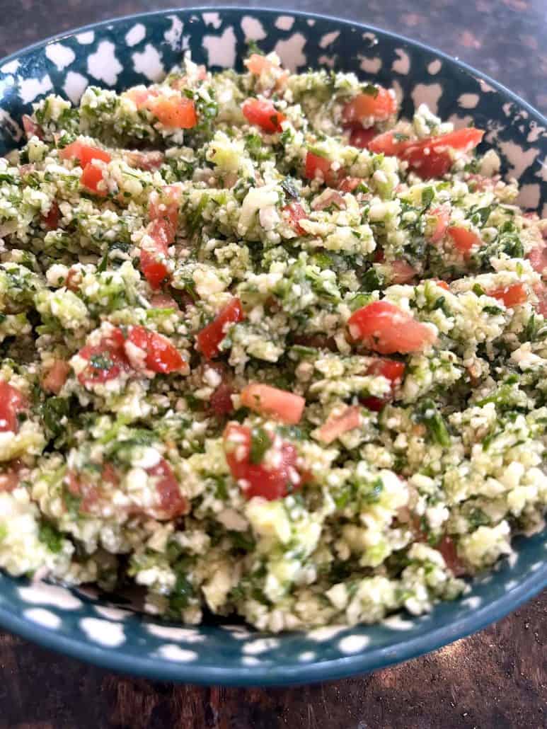 Top view of a colorful cauliflower tabbouleh salad with chopped cauliflower, tomatoes, cucumbers, and parsley in a bowl, garnished with a sprinkle of lemon zest.