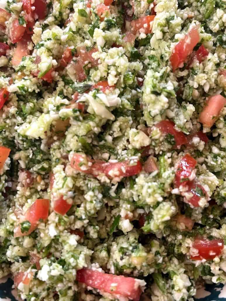 A fresh cauliflower tabbouleh salad featuring chopped parsley, tomatoes, cucumbers, and a zesty lemon dressing.