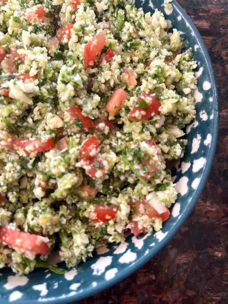 Half view of a cauliflower tabbouleh salad with diced tomatoes, cucumbers, parsley, and cauliflower rice in a bowl with a light lemon garnish