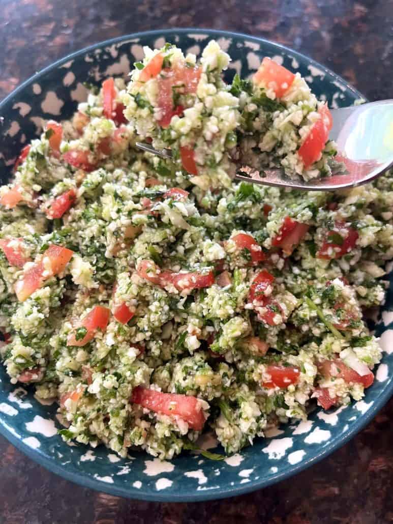 A fresh cauliflower tabbouleh salad featuring chopped parsley, tomatoes, cucumbers, and a zesty lemon dressing.