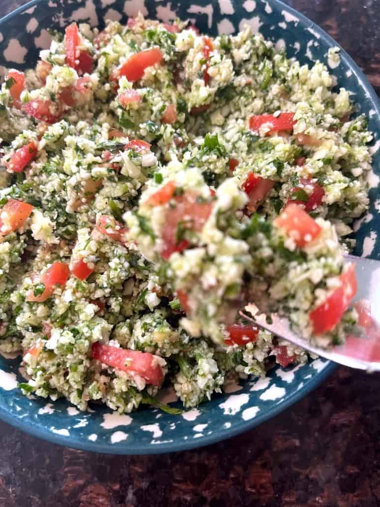 Cauliflower tabbouleh salad with fresh parsley, diced tomatoes, cucumbers, and lemon dressing in a bowl.