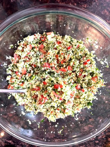 Top view of cauliflower tabbouleh salad in a Pyrex bowl with chopped cauliflower, parsley, tomatoes, cucumbers, and lemon dressing.