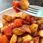 Fried potatoes and tomatoes skewered on a fork.