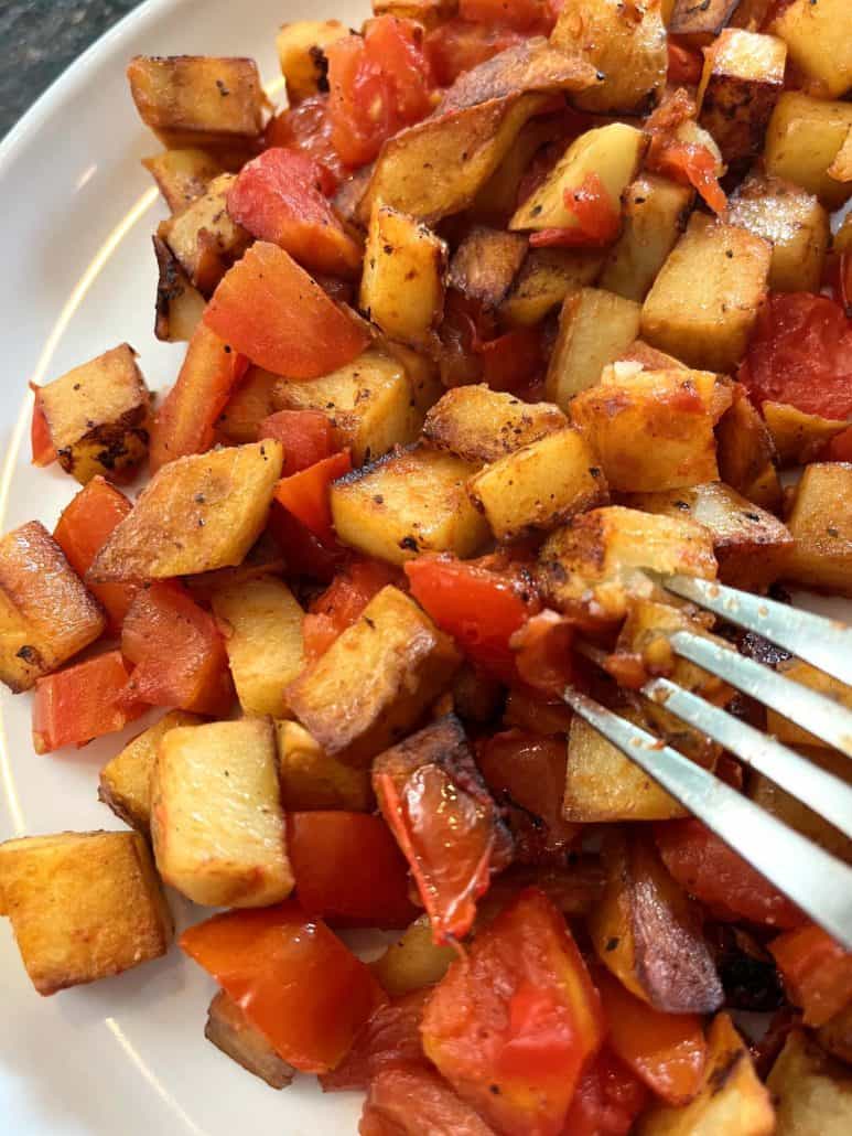 Fried potatoes and tomatoes arranged in a white plate.