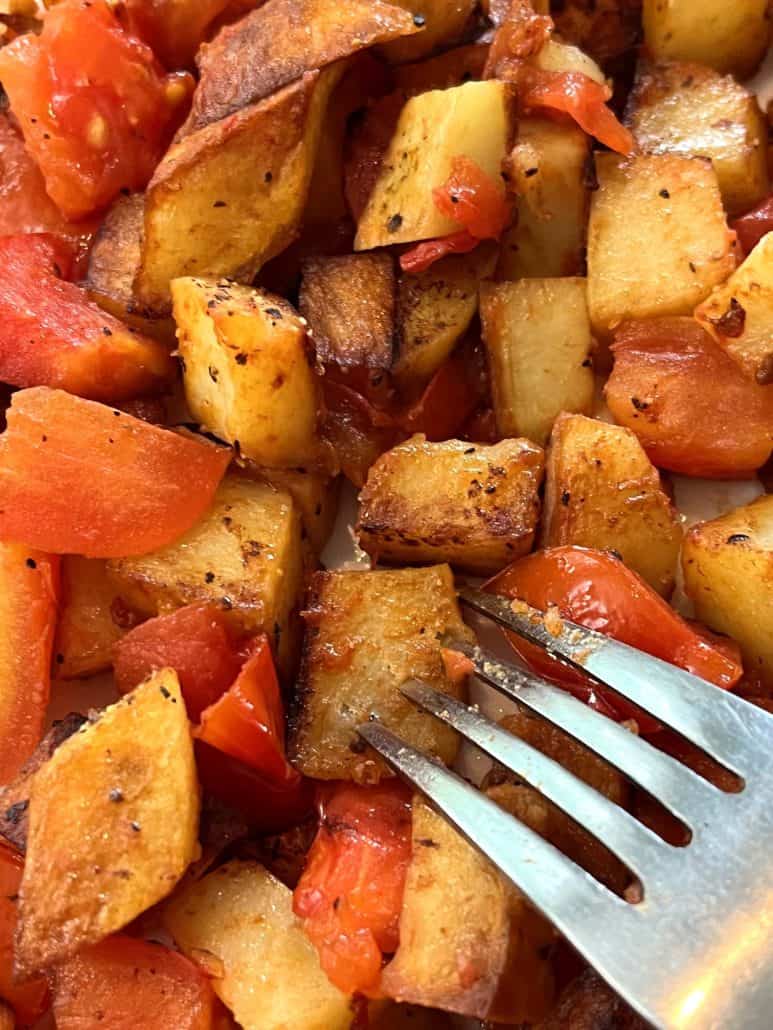 Plate of fried potatoes and tomatoes with seasoning.