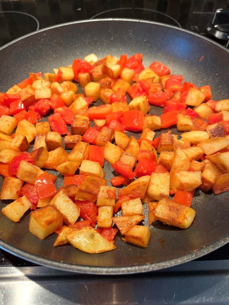 Overhead view of fried potatoes and tomatoes cooking in a non-stick pan.