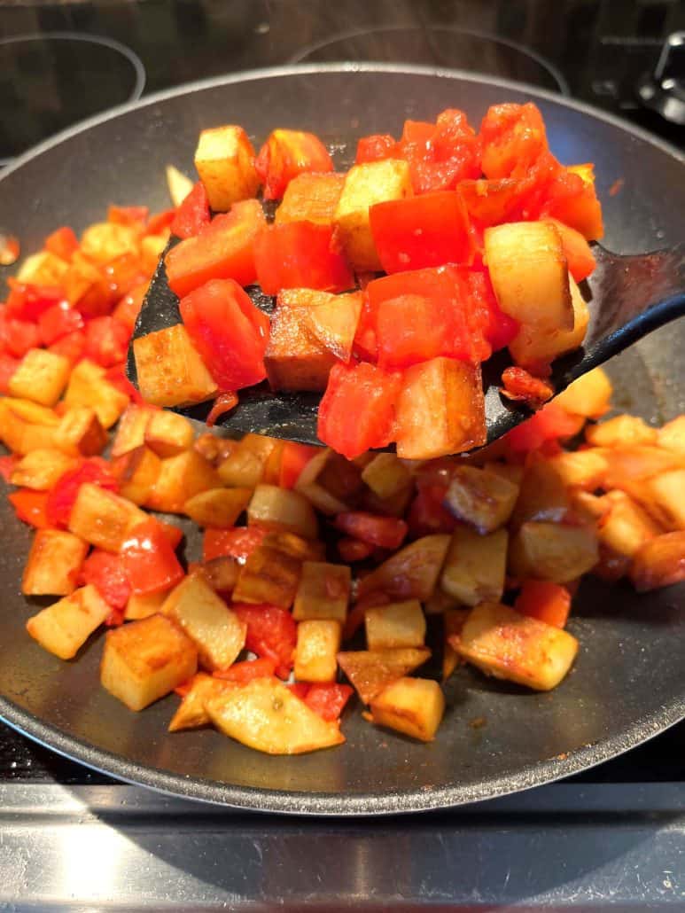 Fried potatoes and tomatoes on a non-stick pan, lifted with a spatula.