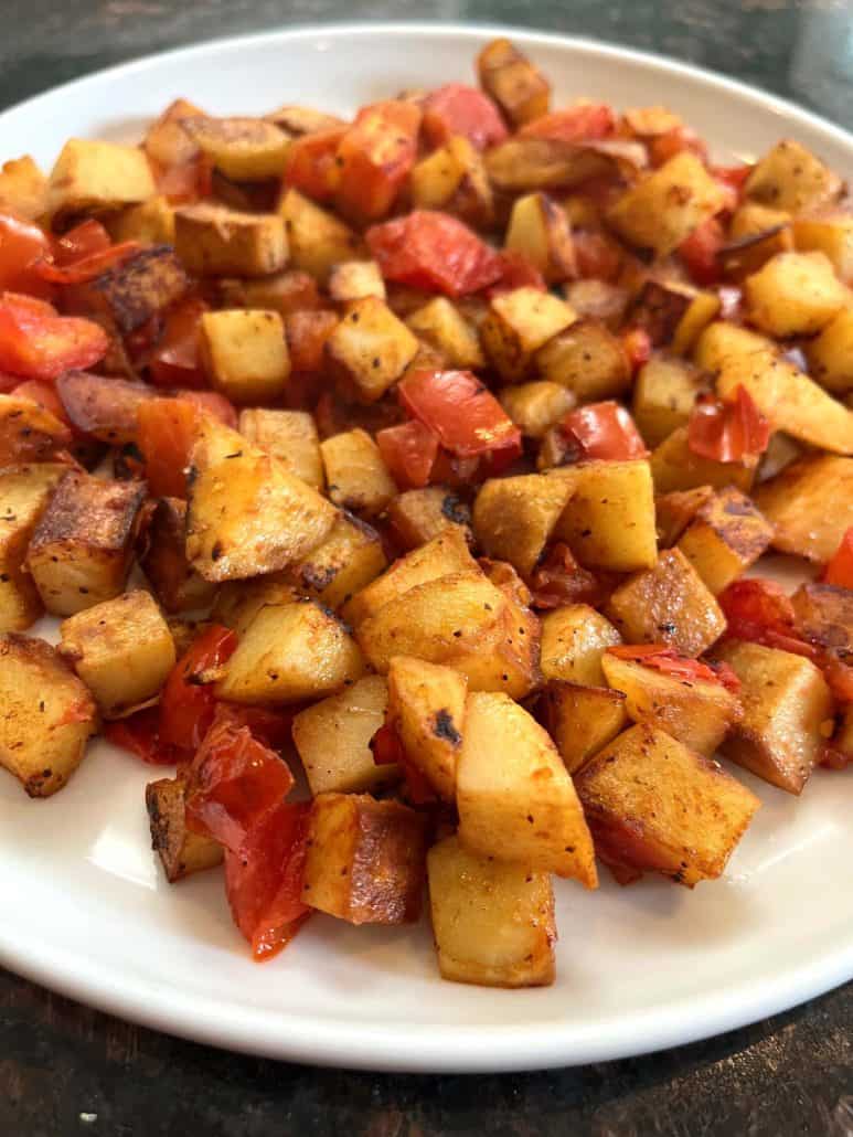 Top view of fried potatoes and tomatoes on a white plate.