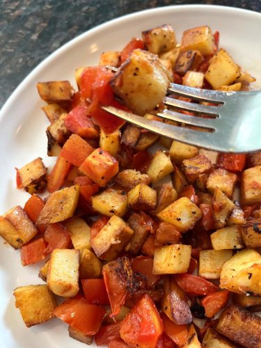 Half shot of fried potatoes and tomatoes skewered on a fork.