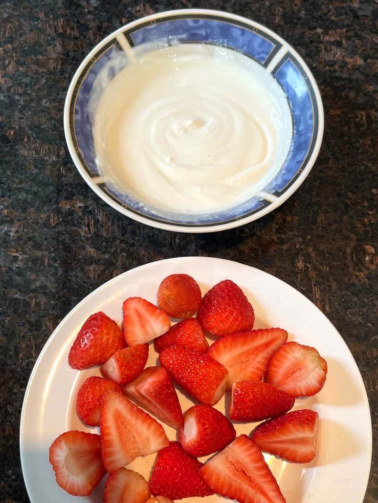 Top view of yogurt in blue saucer and strawberry in white plate.