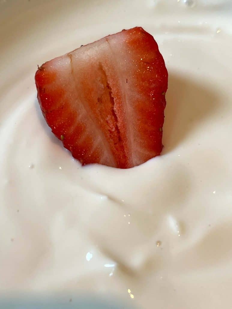 Close-up of creamy yogurt fruit dip with slices of ripe strawberries on top.