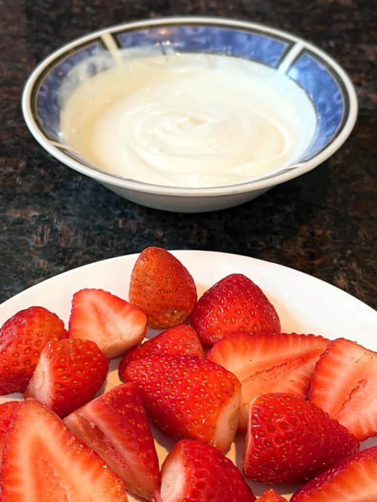 A strawberry in front with yogurt behind.