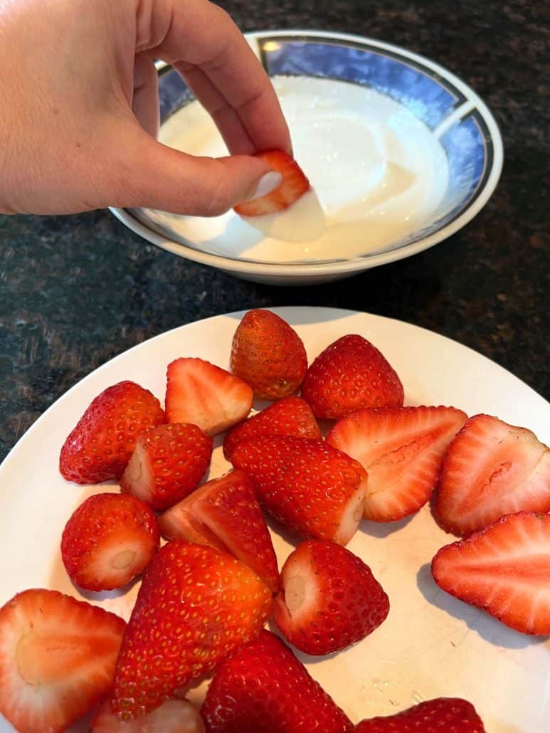 A plate showing yogurt and strawberries in separate sections, with a strawberry coated in yogurt.