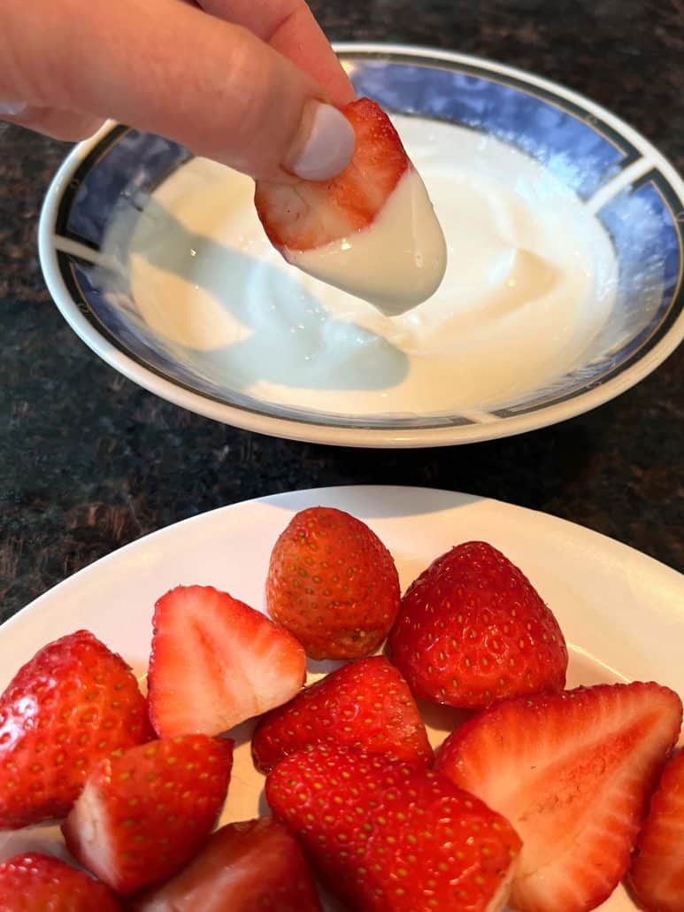 Plate with yogurt and strawberries separately, with a strawberry dipped into the creamy yogurt.