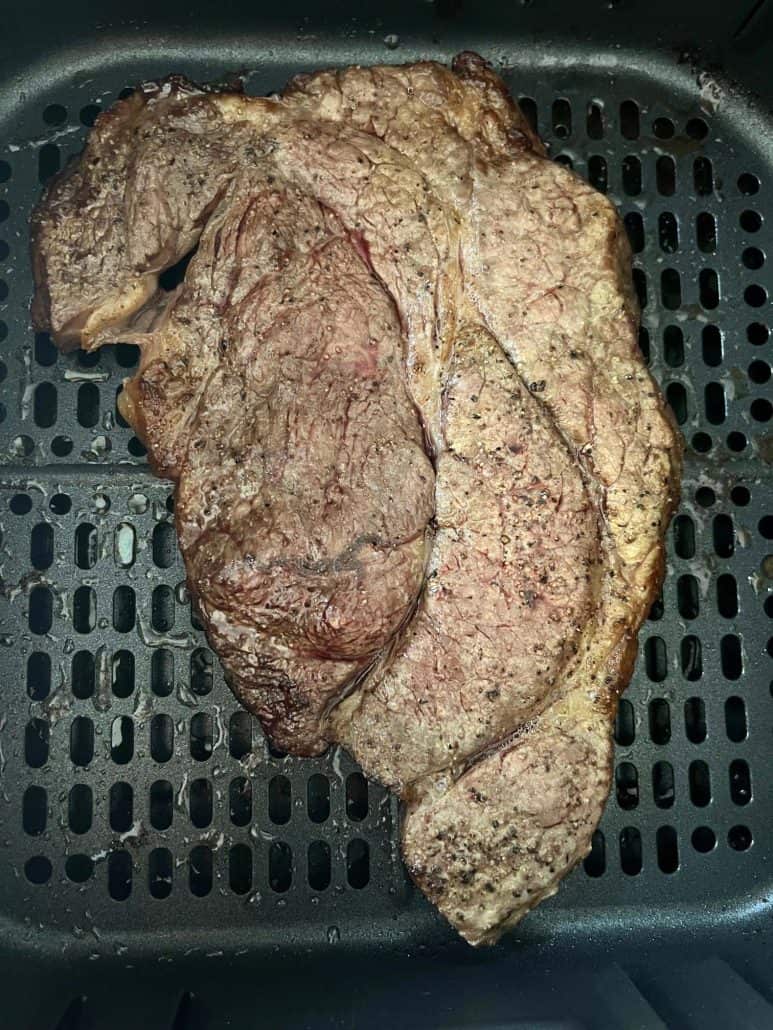 Close-up of a seasoned boneless chuck steak in an air fryer basket, perfectly cooked with a golden-brown crust.