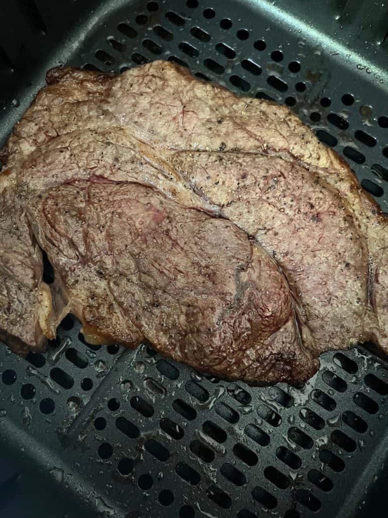 Boneless chuck steak with a perfectly browned exterior, resting in an air fryer basket after cooking.