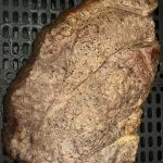 Boneless chuck steak with a seasoned, browned crust, resting in an air fryer basket after cooking.