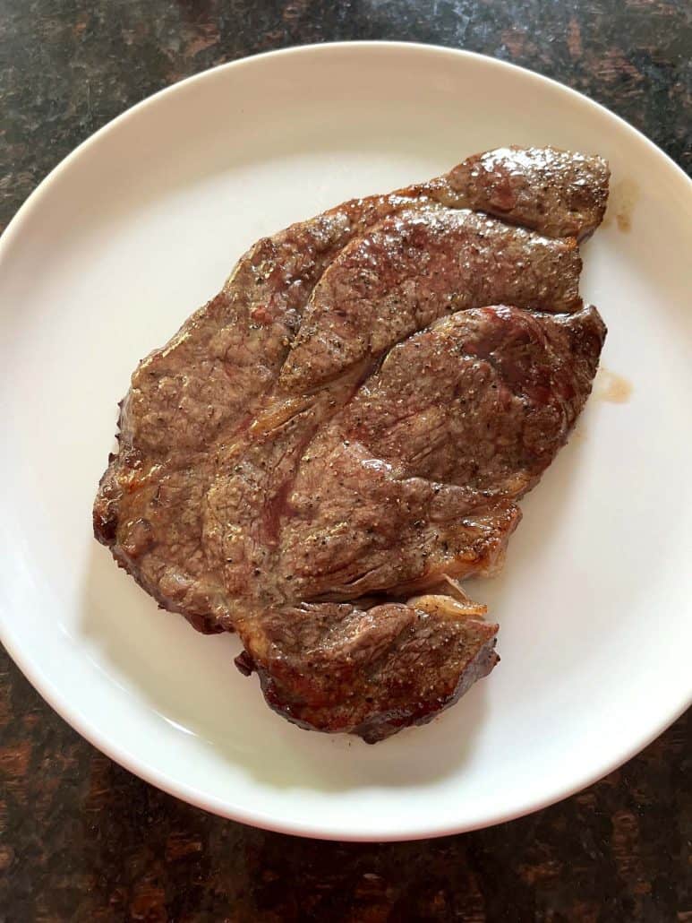 Perfectly cooked boneless chuck steak on a white plate, showcasing a juicy and tender finish after air frying.