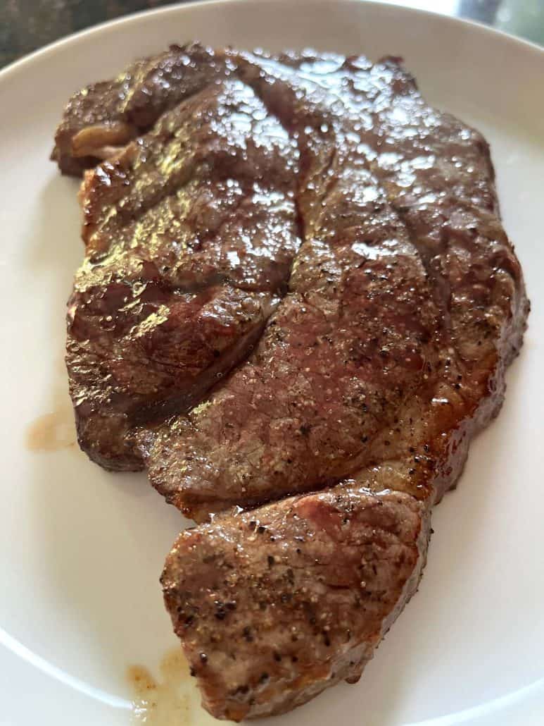 Close-up of a juicy boneless chuck steak on a white plate, highlighting the seared, seasoned exterior achieved with air frying.