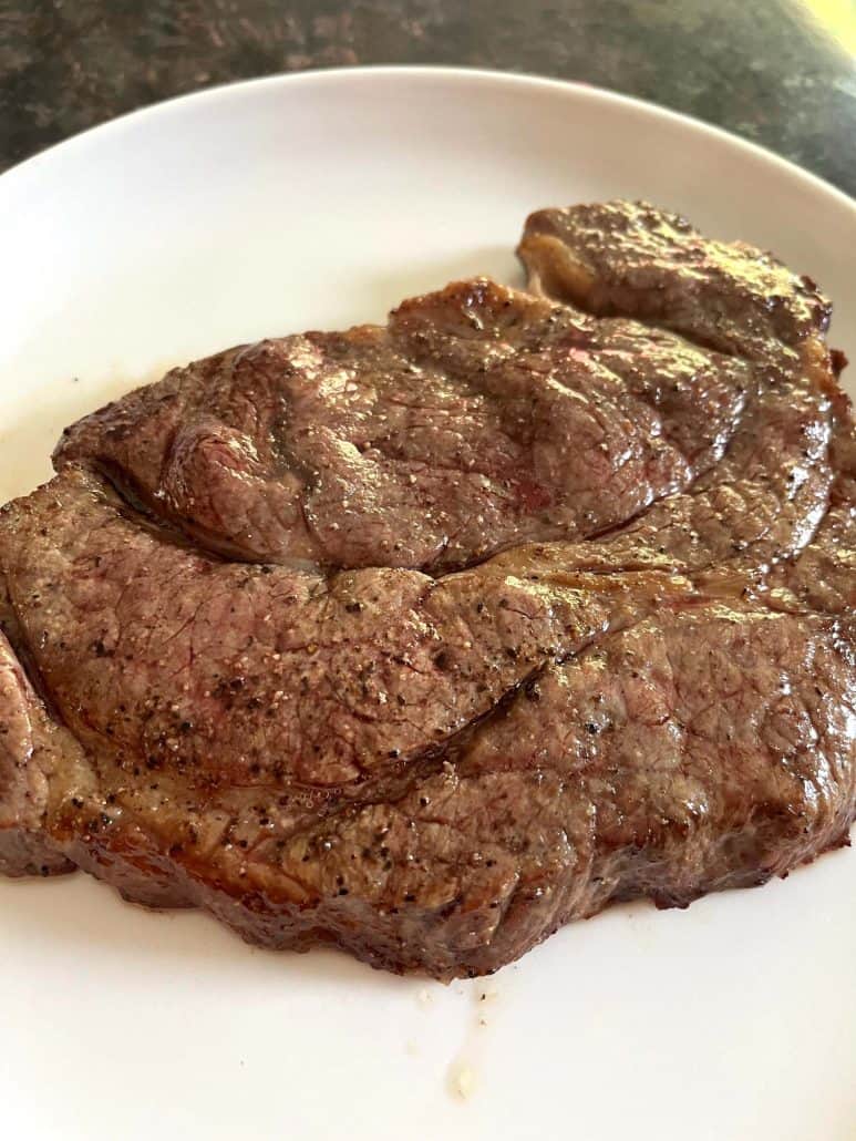 Cooked boneless chuck steak on a white plate, highlighting its tender, juicy texture and rich, seasoned crust.