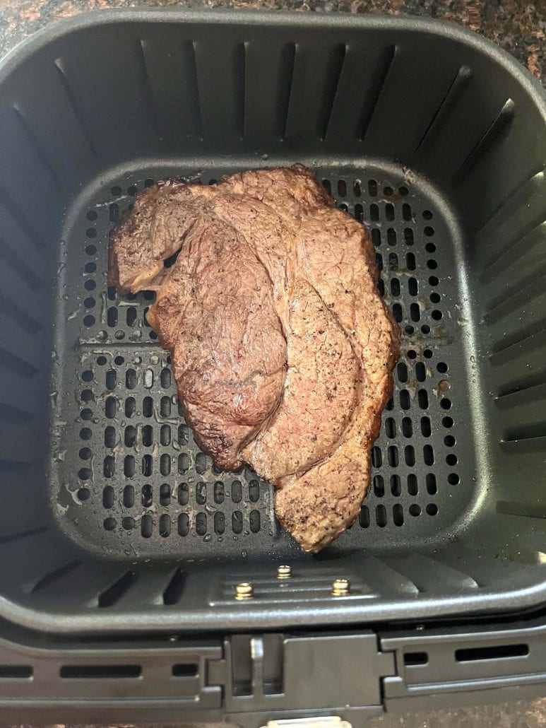 Cooked boneless chuck steak resting in an air fryer basket, showcasing its golden-brown, perfectly seared exterior.